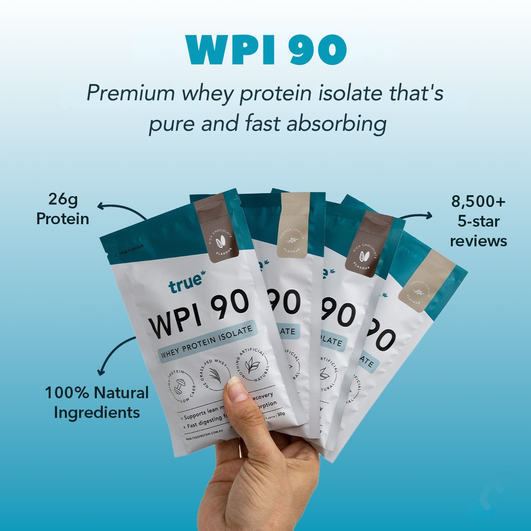 Hand holding four True WPI 90 whey protein isolate sample sachets on blue background — 26g protein, 100% natural ingredients, fast-absorbing premium whey, 8,500+ 5‑star reviews, Australian brand.