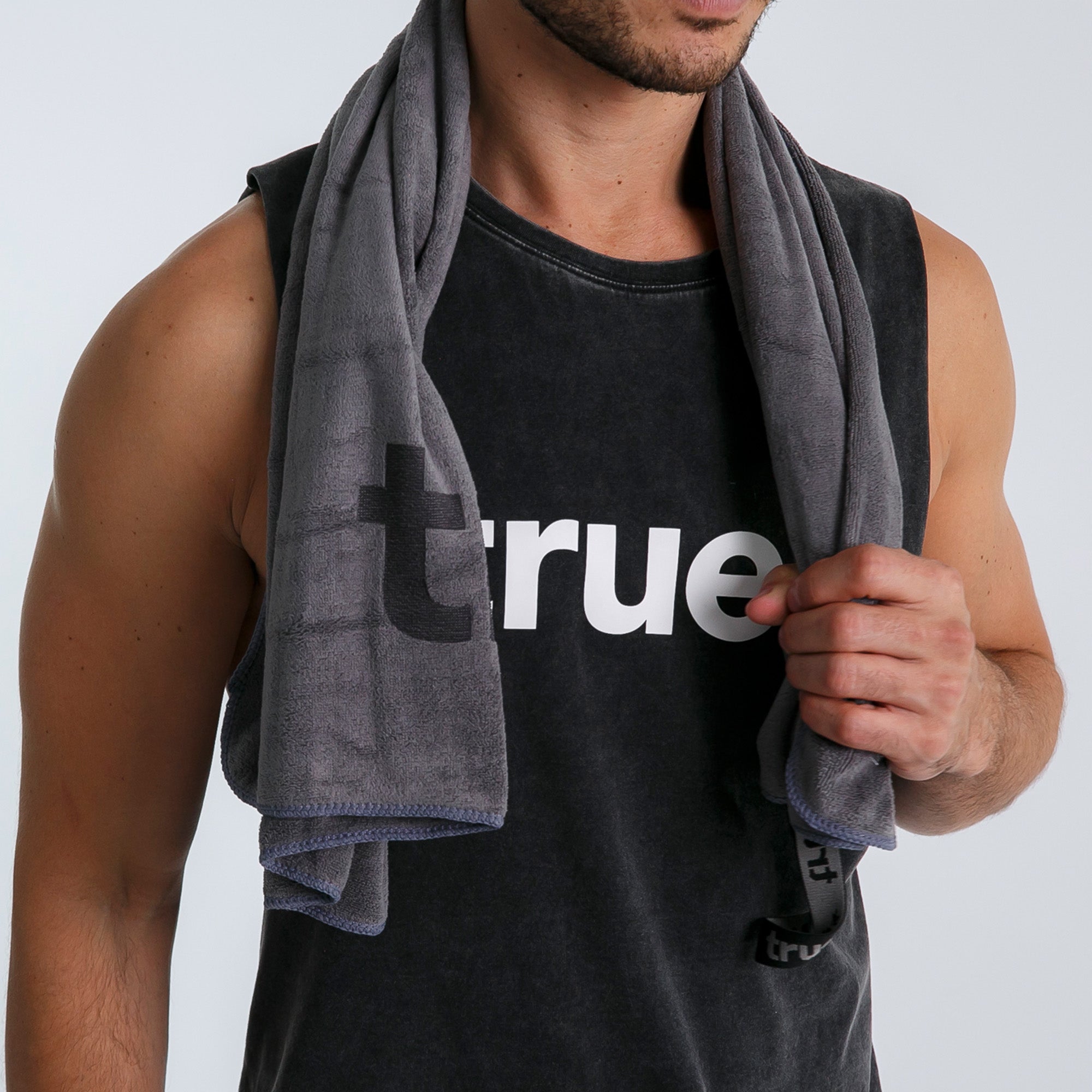 Gray microfiber gym towel draped over shoulders of male model wearing black "true" tank top — absorbent workout towel for gym, fitness and travel