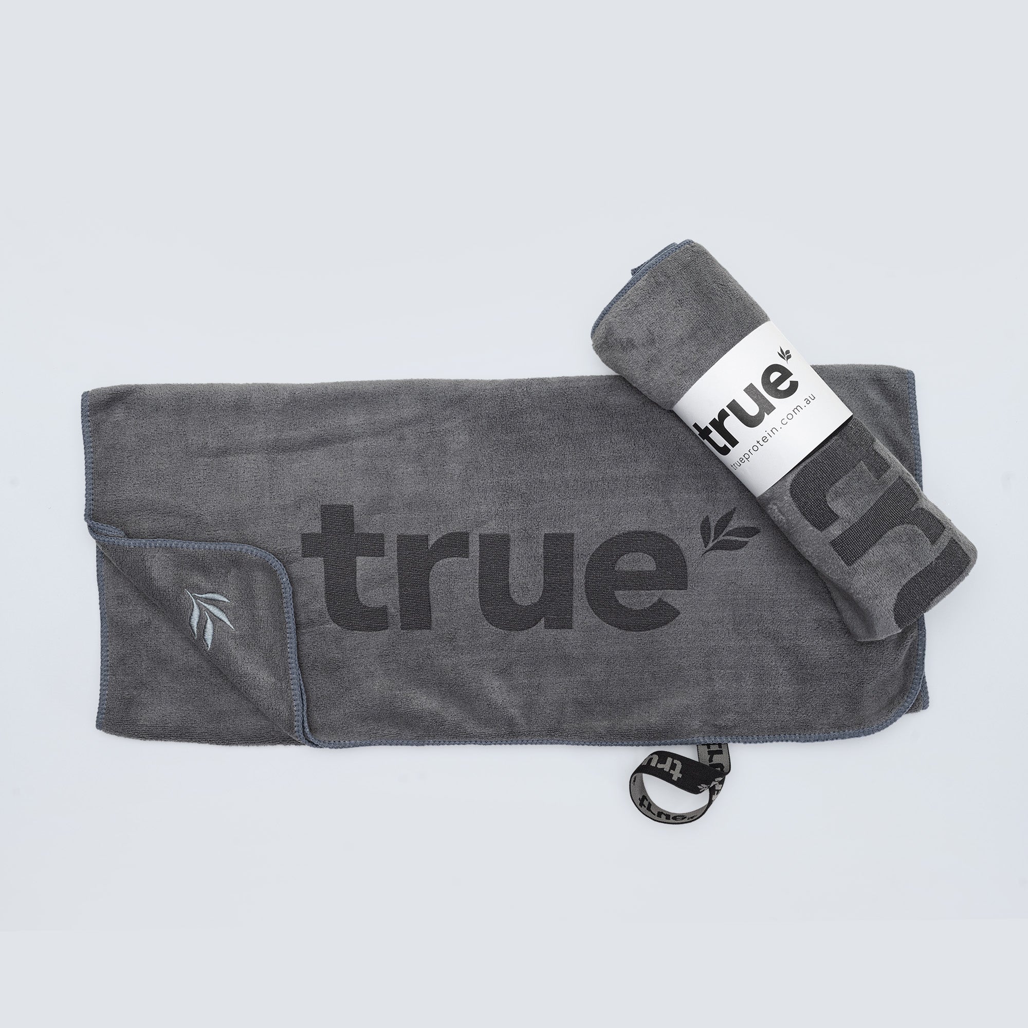 Charcoal grey microfiber gym towel with large "true" logo and embroidered leaf, rolled and flat, True Protein branded towel (Australia)