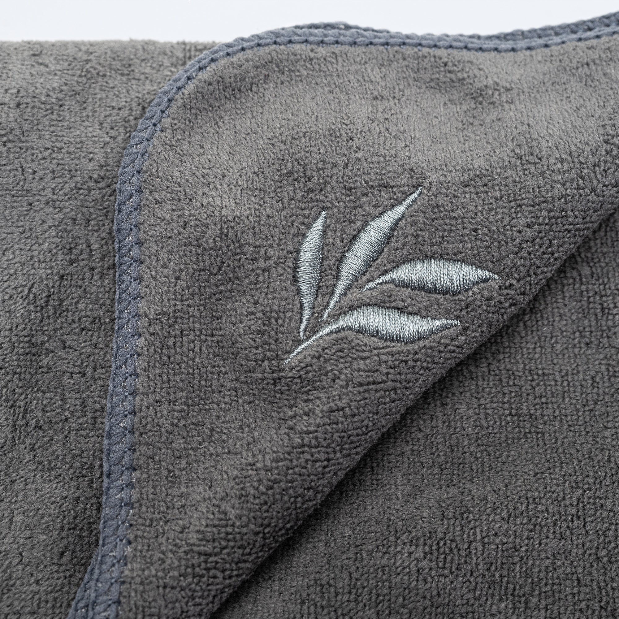 Close-up of charcoal grey microfiber gym towel with navy stitched edge and light grey embroidered leaf logo — soft, absorbent fitness towel for gym, yoga, travel.