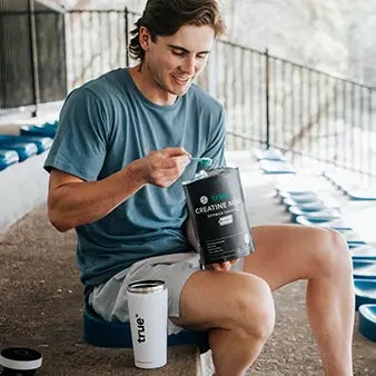 Young man on outdoor stadium bleachers scooping True brand creatine monohydrate supplement for lean muscle and workout recovery