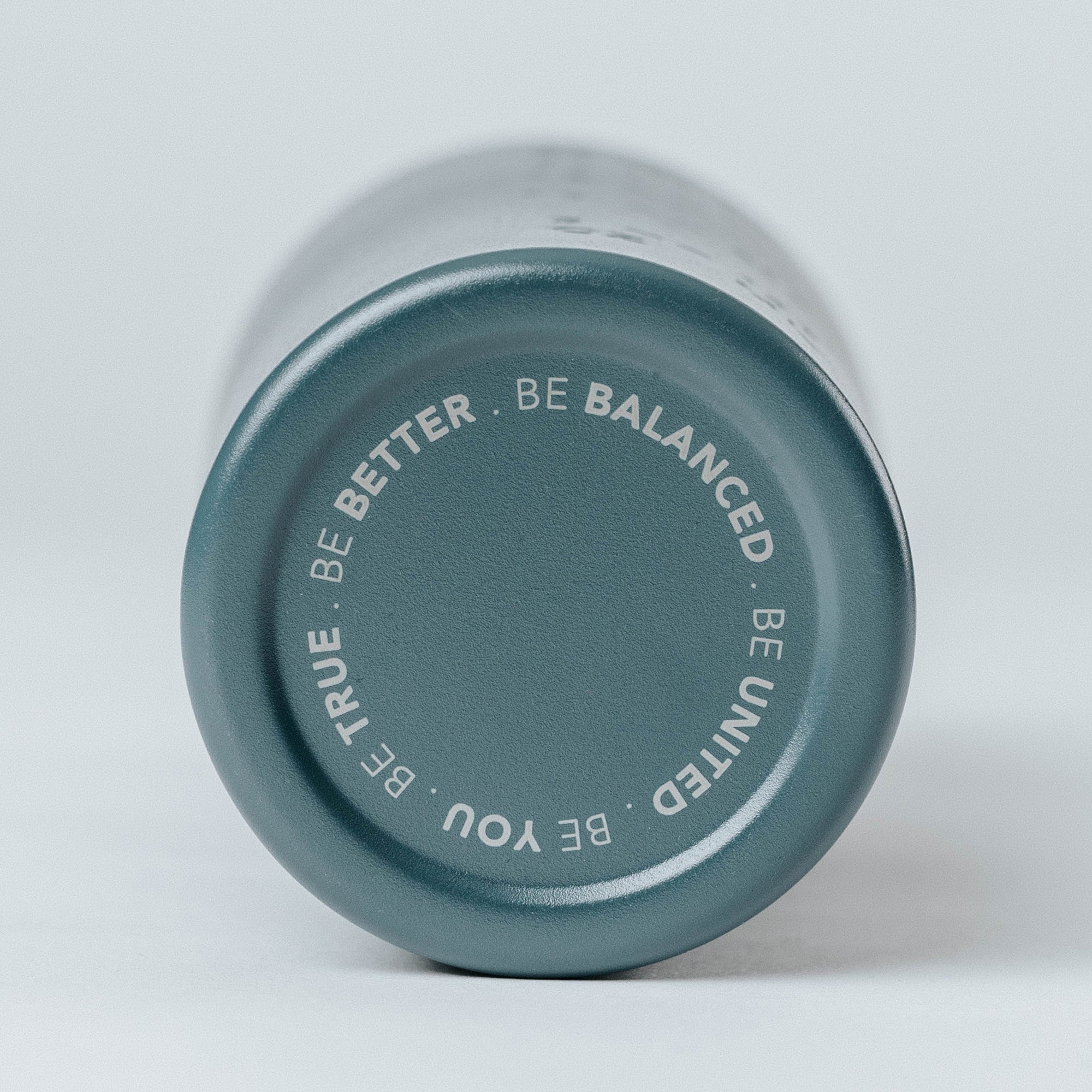 Navy matte stainless-steel shaker bottle bottom view with circular white text “BE BETTER · BE BALANCED · BE UNITED · BE TRUE · BE YOU” – fitness water bottle, gym shaker, product shot on light background