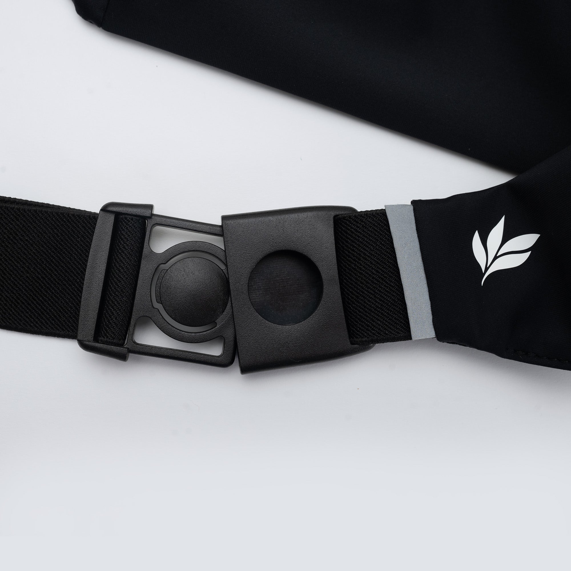 Close-up of black running belt adjustable buckle and strap with reflective trim and white leaf logo — slim waist pack for runners.