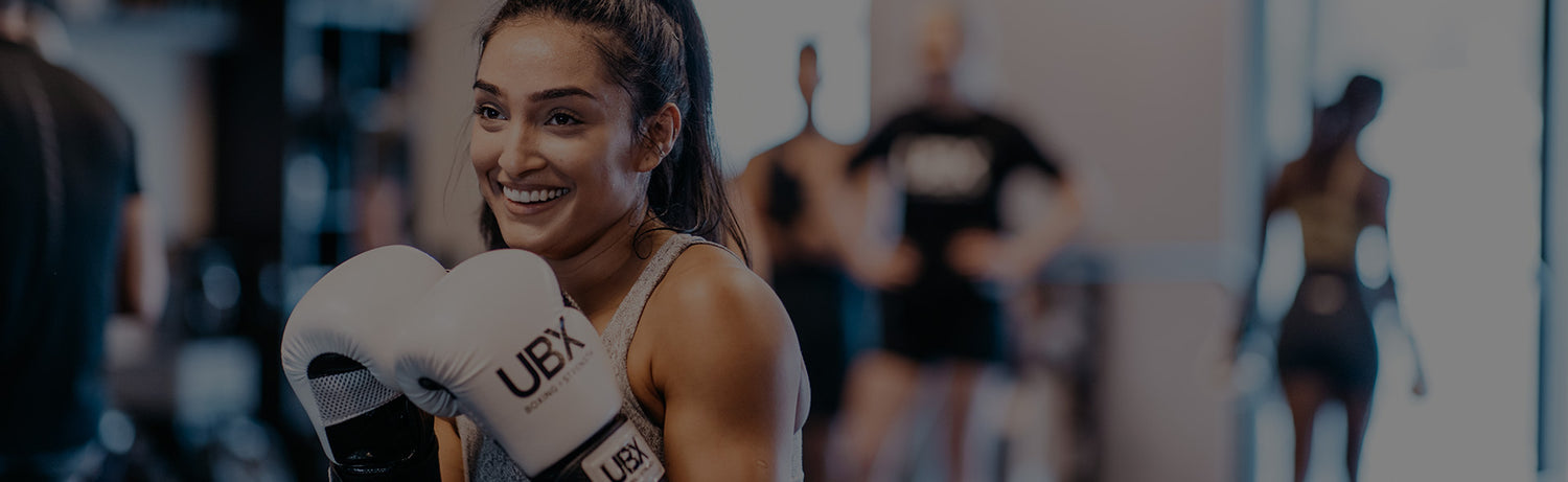 Smiling woman wearing UBX boxing gloves during a group UBX boxing studio class in a modern gym
