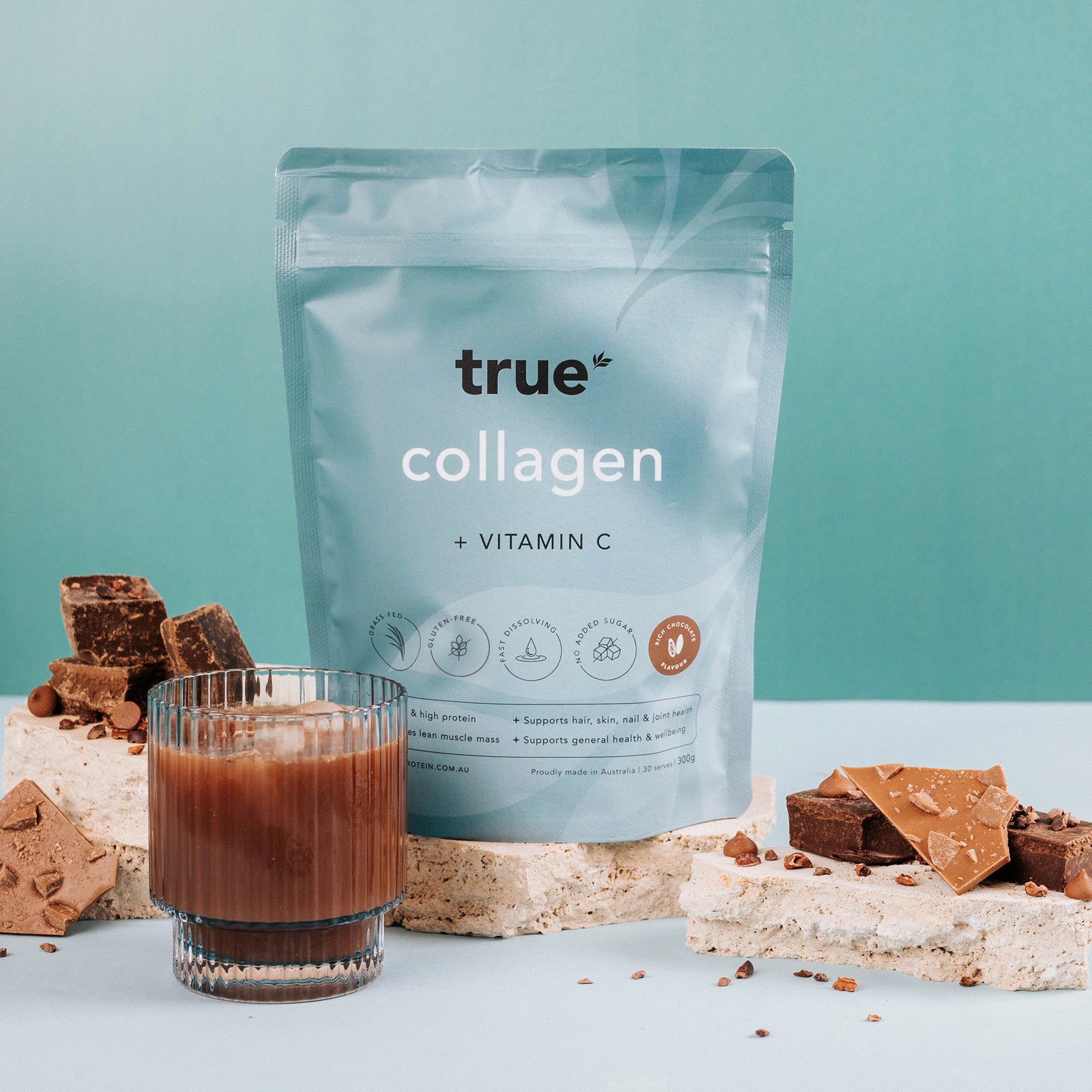 True Collagen + Vitamin C chocolate-flavoured powder pouch with chocolate pieces and a glass of prepared chocolate collagen drink on teal background — Australian-made collagen supplement.