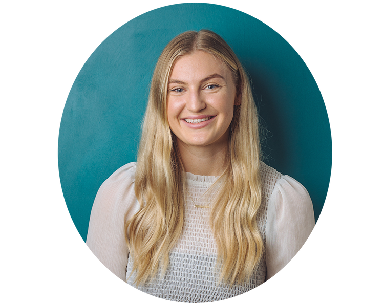 Studio headshot of a smiling young woman with long blonde hair wearing a white textured blouse against a teal background, professional portrait for wellness brand or team page.
