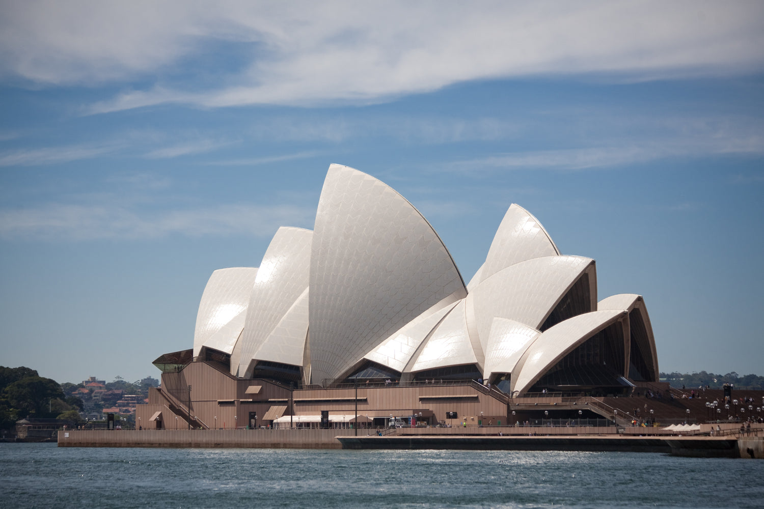 Sydney Opera House with its white sail-like shells on Sydney Harbour waterfront, Sydney, Australia — clear sky and harbor foreground.