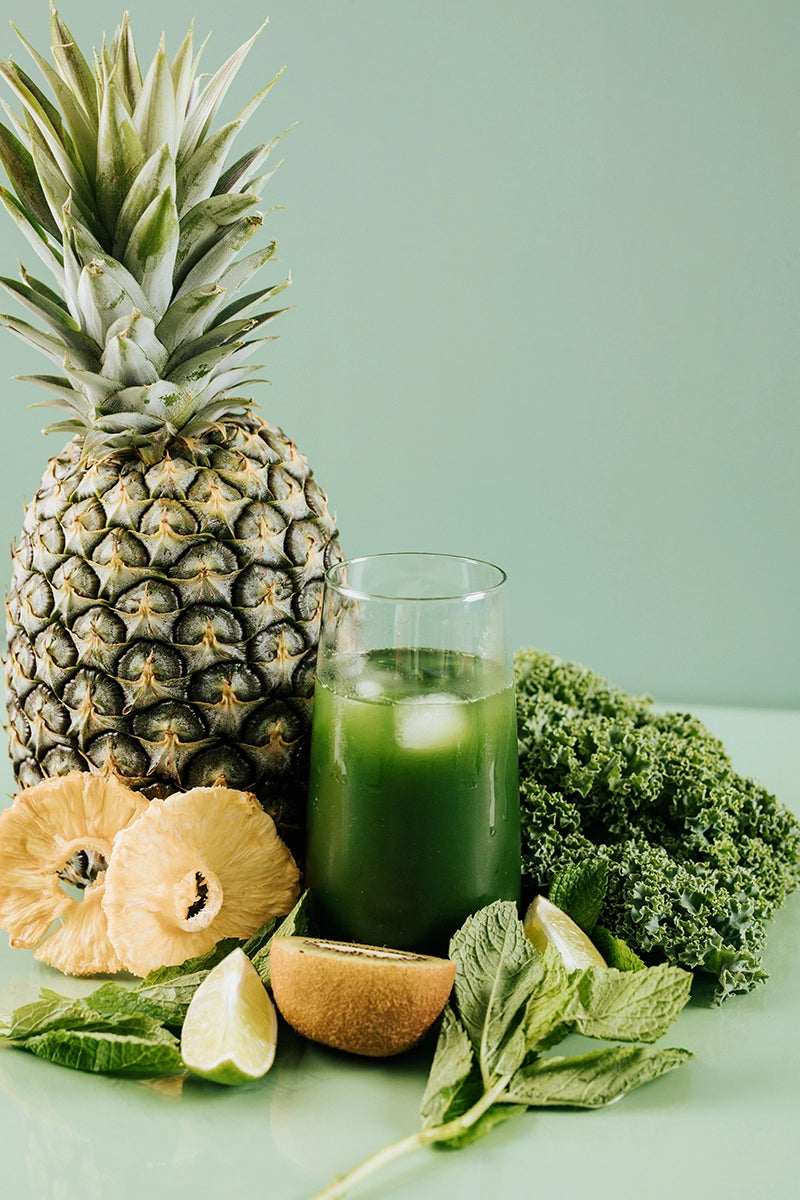 Pineapple, green juice, kale, and lime on a light green background - True Protein Greens