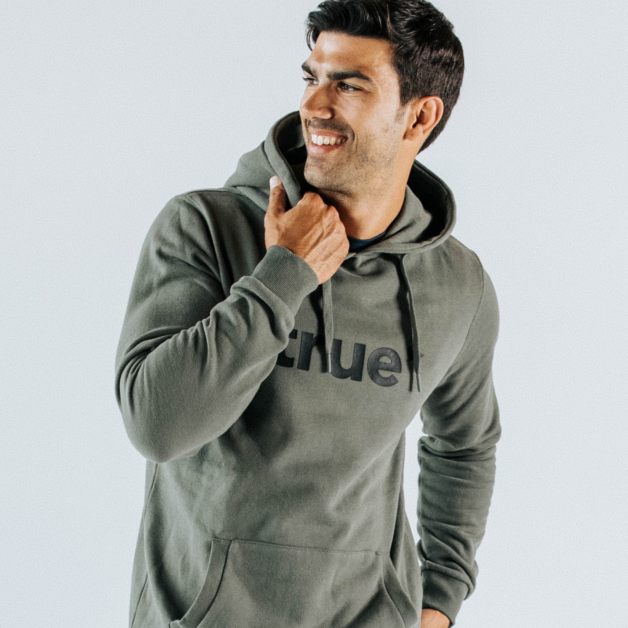 Male model wearing khaki pullover hoodie with drawstring hood, kangaroo pocket and black front "true" logo — casual men&