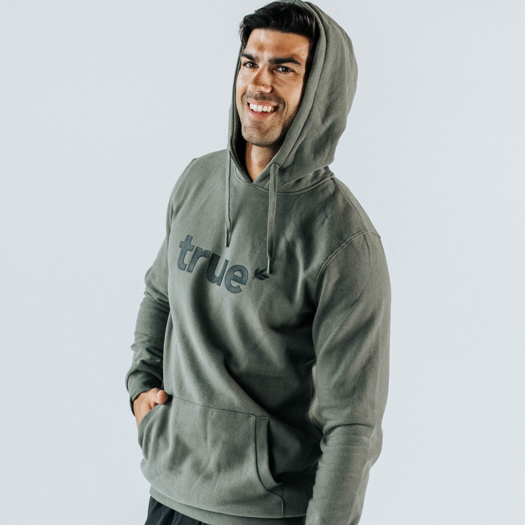 Smiling male model wearing khaki green "true" pullover hoodie with kangaroo pocket, front view studio shot — men&