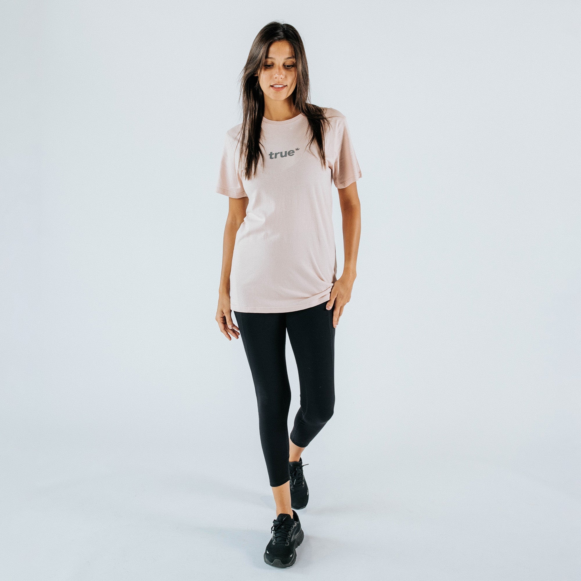 Female model in studio wearing a blush pink "true" logo t-shirt with a relaxed fit and black cropped leggings, black sneakers — women&