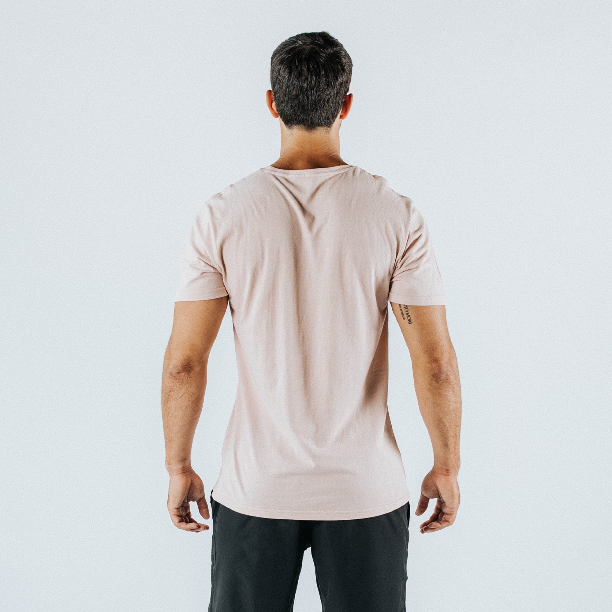 Back view of male model wearing pale pink slim-fit crewneck t-shirt and black shorts on plain white studio background — casual men’s summer tee product photo, Los Angeles e-commerce garment image.