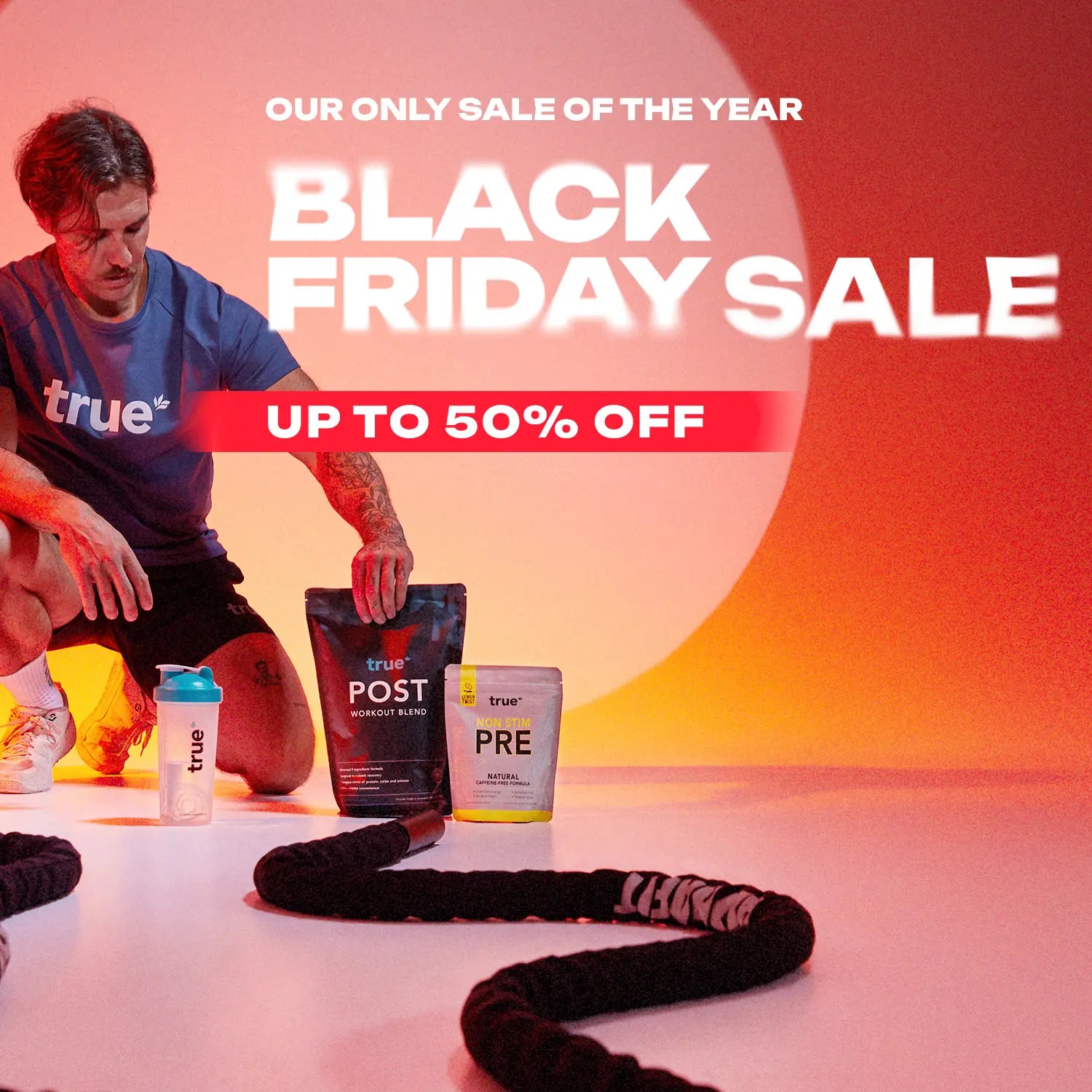 Black Friday sale banner for True workout supplements — "Up to 50% off" text with a man in a True t‑shirt, True shaker bottle, True Post workout blend and Non‑Stim PRE packets on a gym floor with battle ropes.