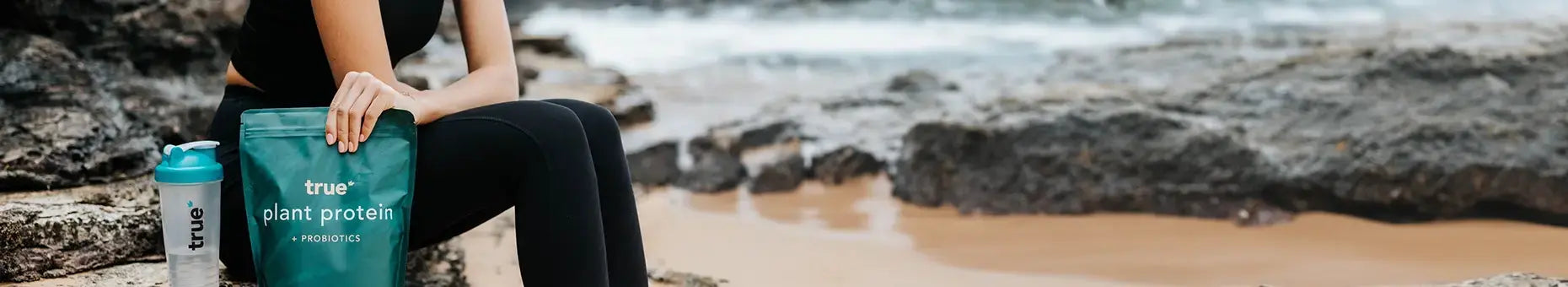Person sitting on a rock by the ocean with a protein powder bag and water bottle.