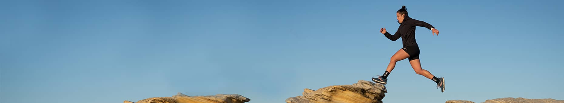 Person running on a rocky outcrop with a clear blue sky