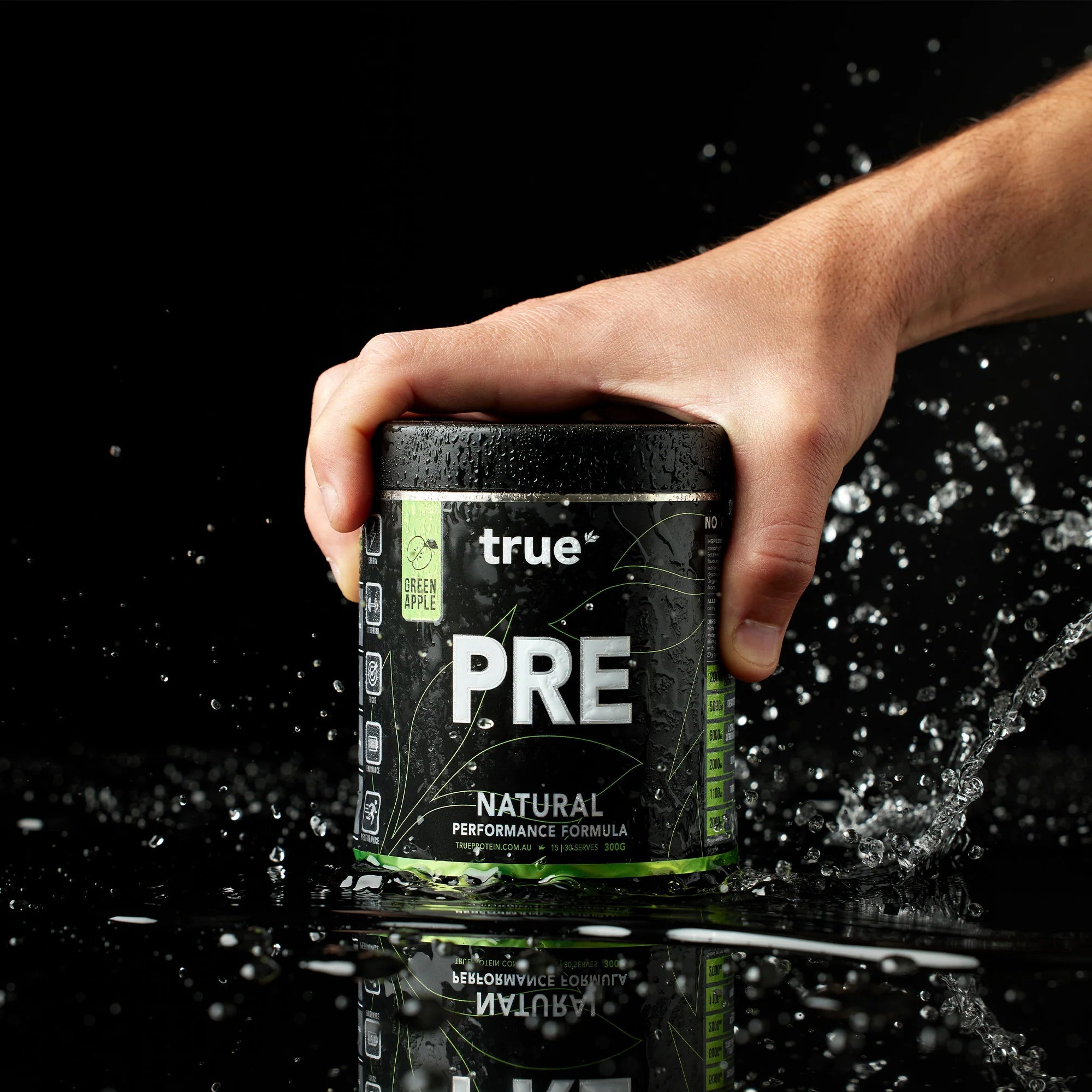 True PRE natural performance pre-workout supplement tub (Green Apple) by True, hand holding product with water splash on black background — product shot, suitable for Australia e-commerce.