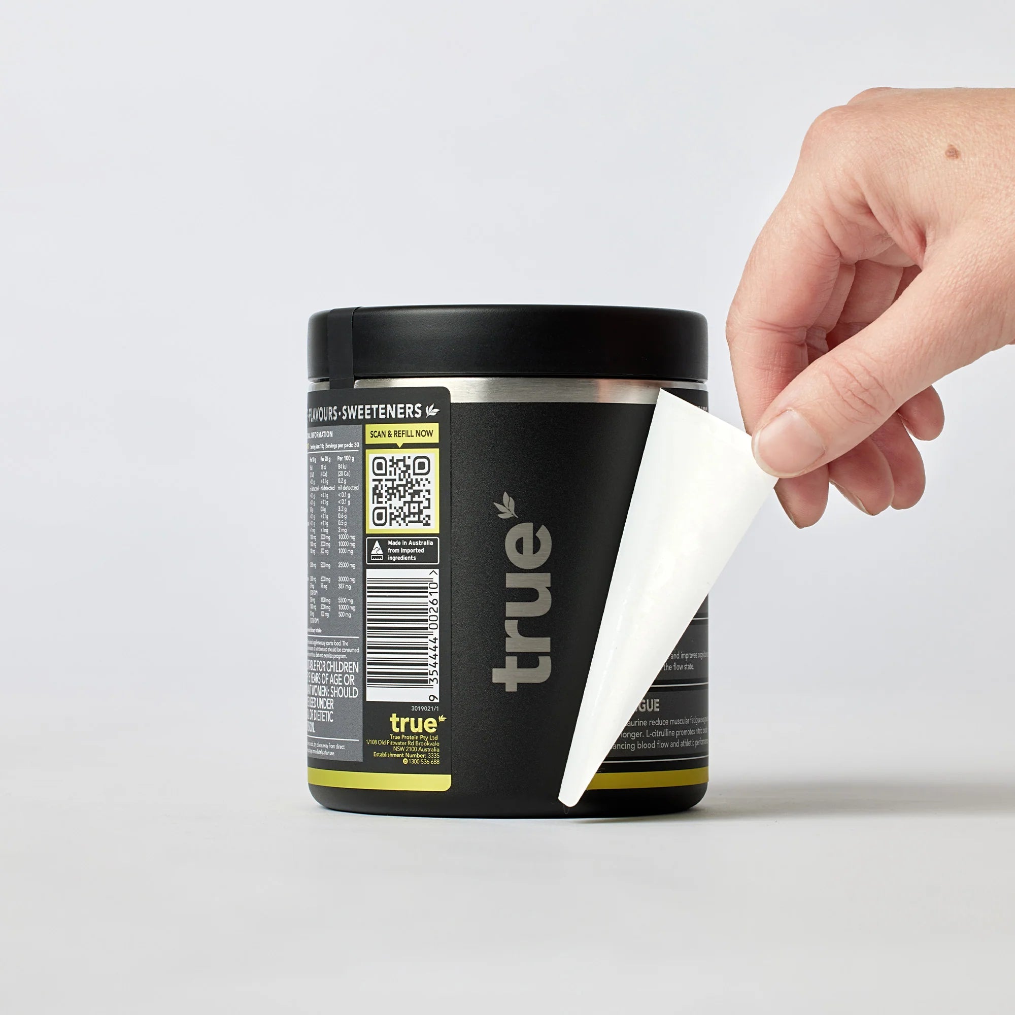 Black "True" pre-workout supplement tub with hand peeling off label, close-up product packaging for fitness supplements, Australian-made jar on white background