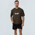 Male model in brown oversized unisex cotton T‑shirt with white "true" logo and black "true" shorts on light studio background — casual streetwear product shot, front view.