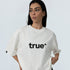Female model wearing white unisex oversized cotton t-shirt with black "true" logo, front product shot on light gray background.