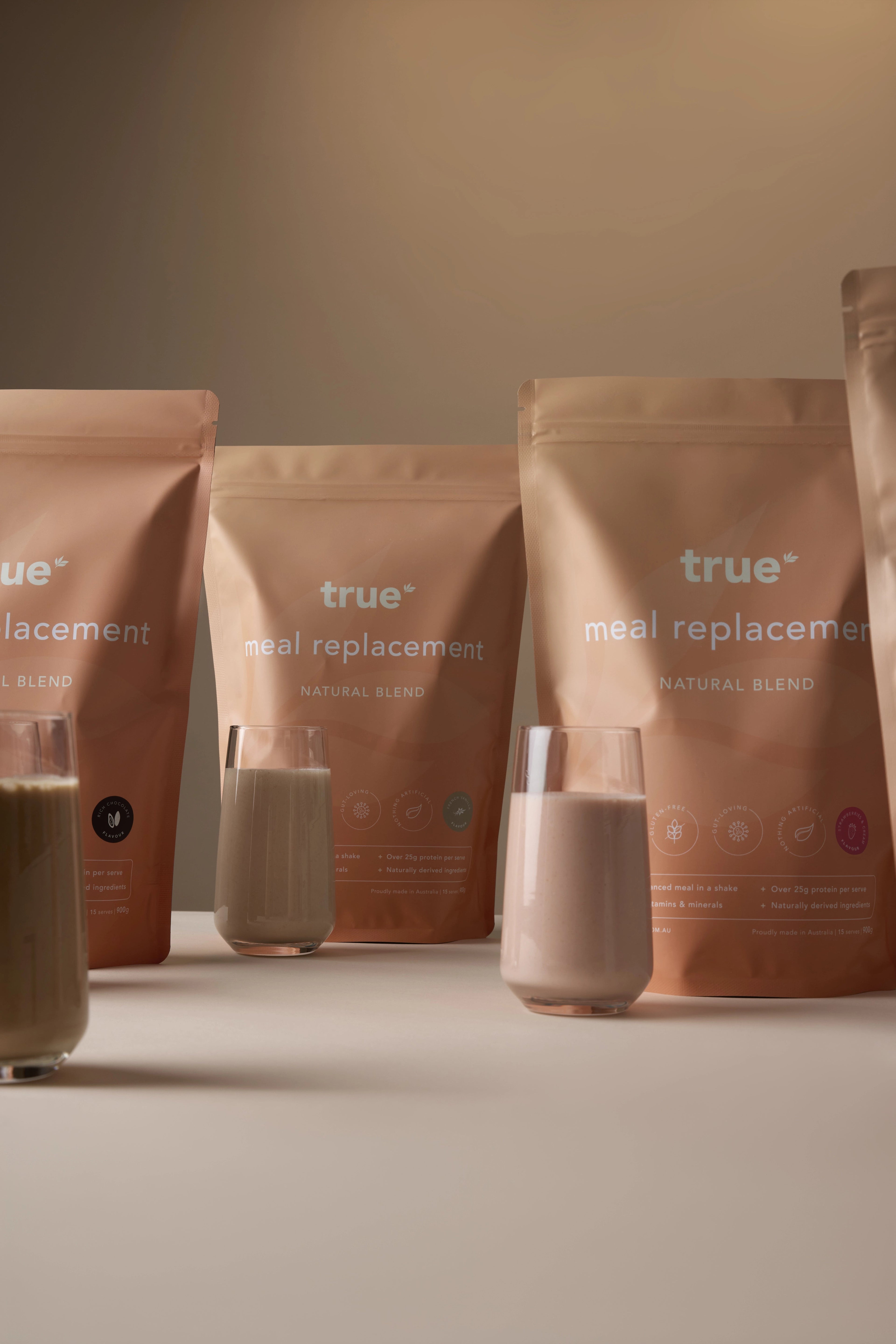 True meal replacement natural blend pouches with three glasses of prepared protein shakes on a neutral background — Australian-made meal replacement powder product photo, perfect for weight management and nutrition.