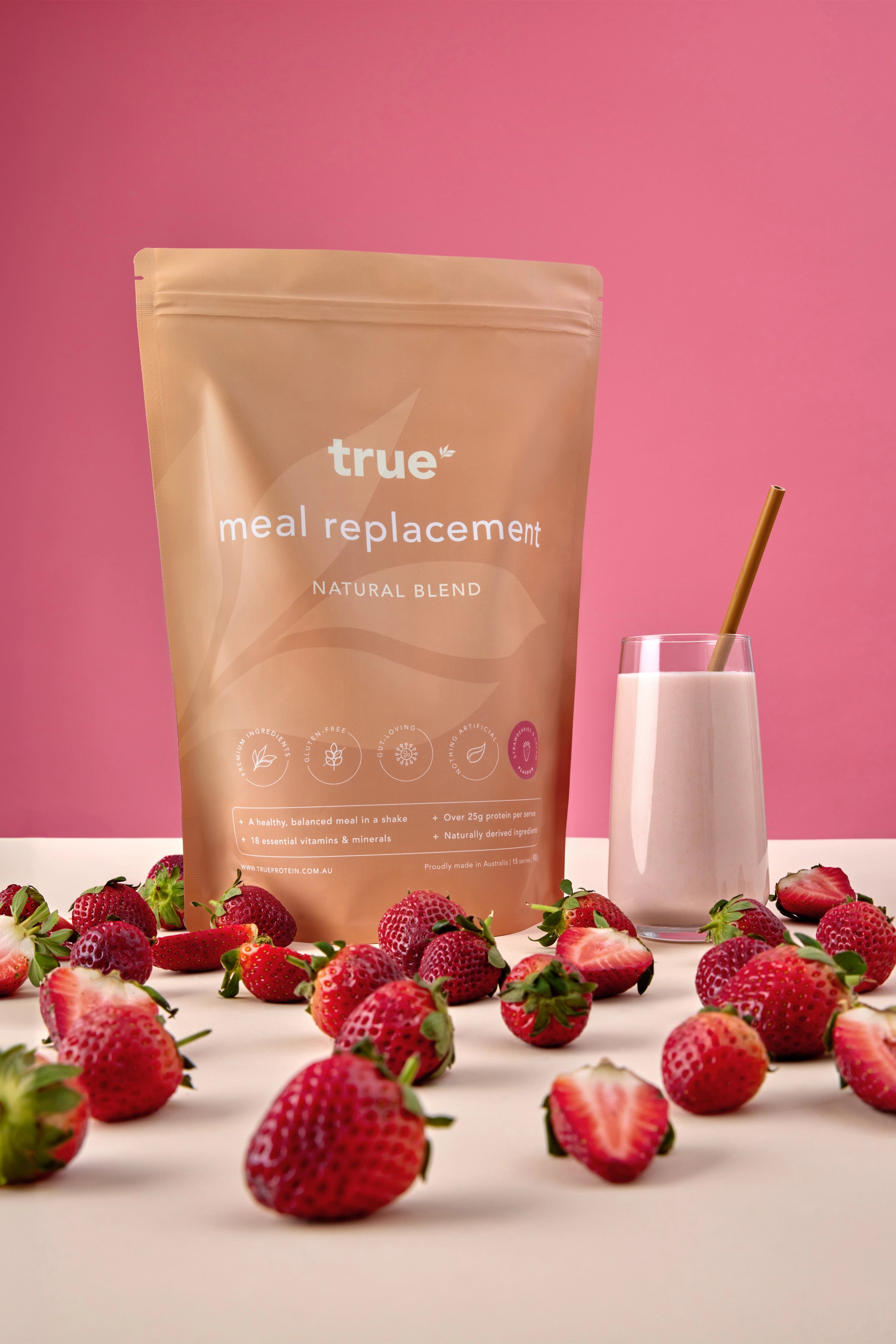 True Protein meal replacement natural blend — strawberries &amp; cream flavour pouch with glass of strawberry shake and fresh strawberries on pink background, Australian-made.
