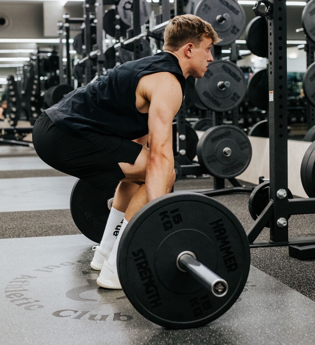 Man in a black singlet setting up for a barbell deadlift in a gym