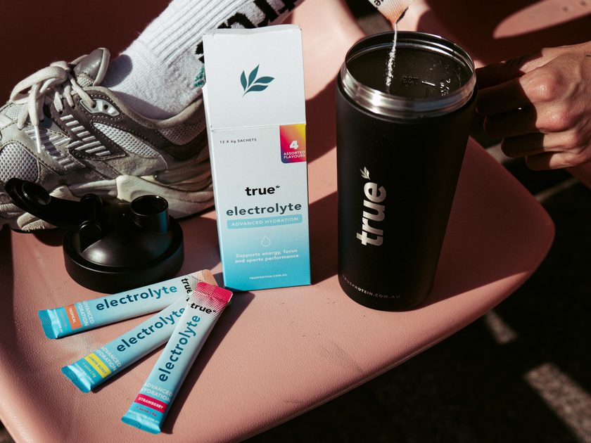 True Electrolyte Travel Pack box with Tropical, Lemon Burst and Strawberry sachets beside a True shaker as a sachet is poured in