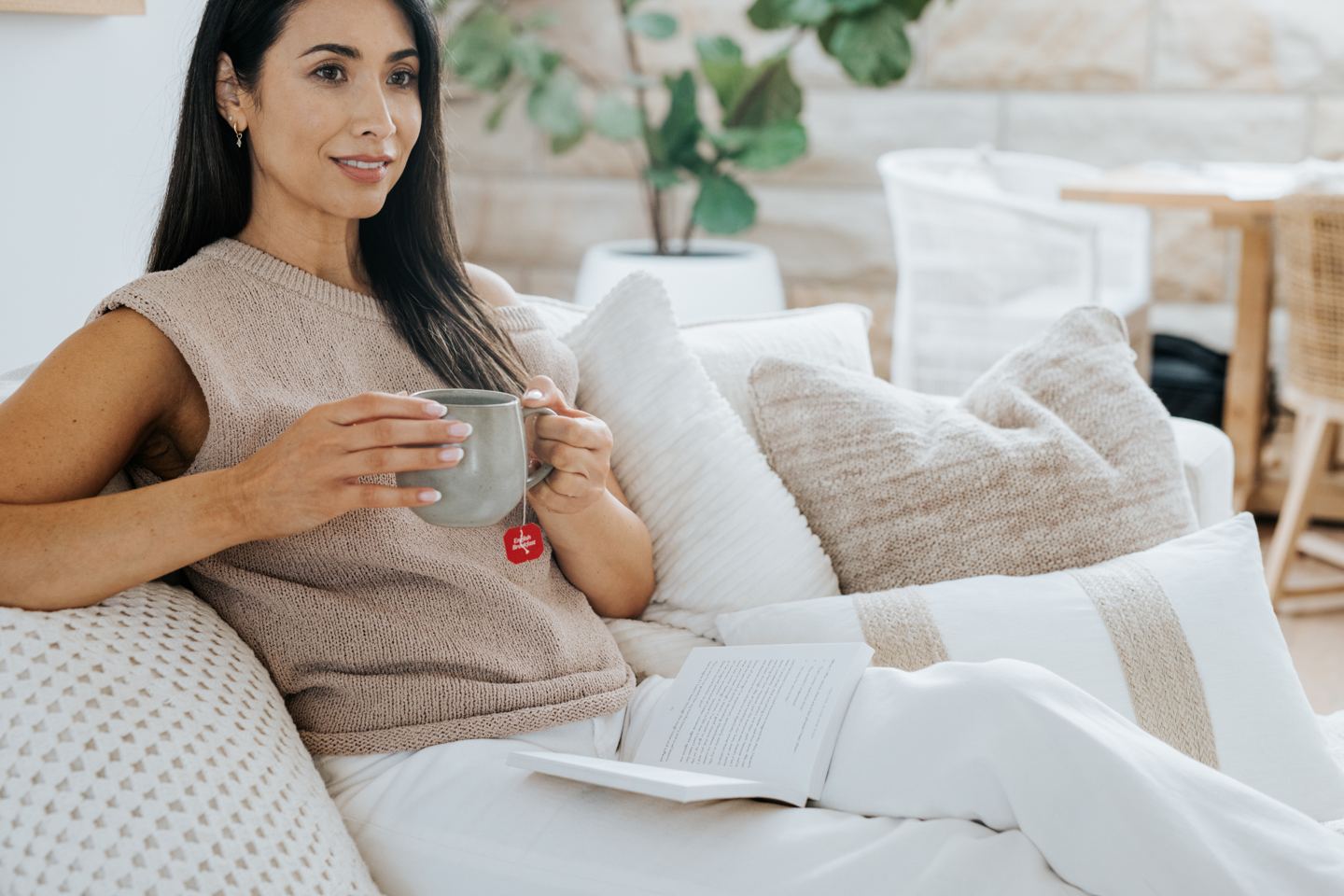 Woman relaxing on a couch at home with a mug of tea and a book