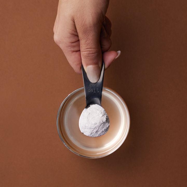 A level teaspoon of Magnesium+ powder held over a glass of water