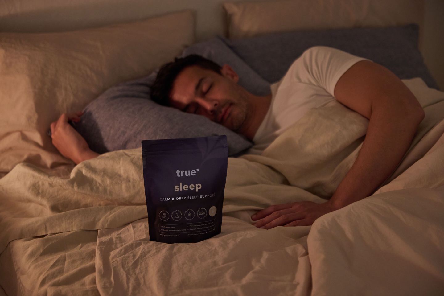 A man asleep in bed at night with a pouch of True Sleep on the covers