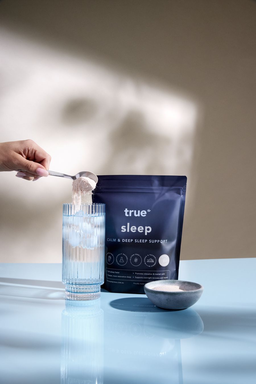 Spooning True Sleep powder into a glass of iced water beside the 300g pouch