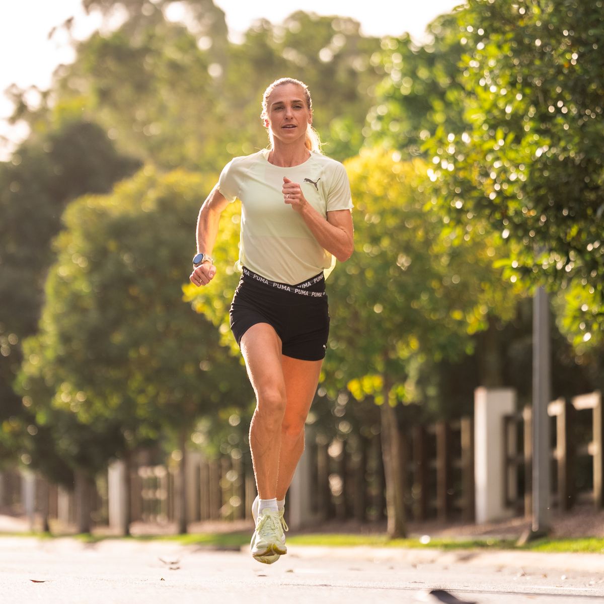 A runner heading straight towards the camera on a sunlit, tree-lined street